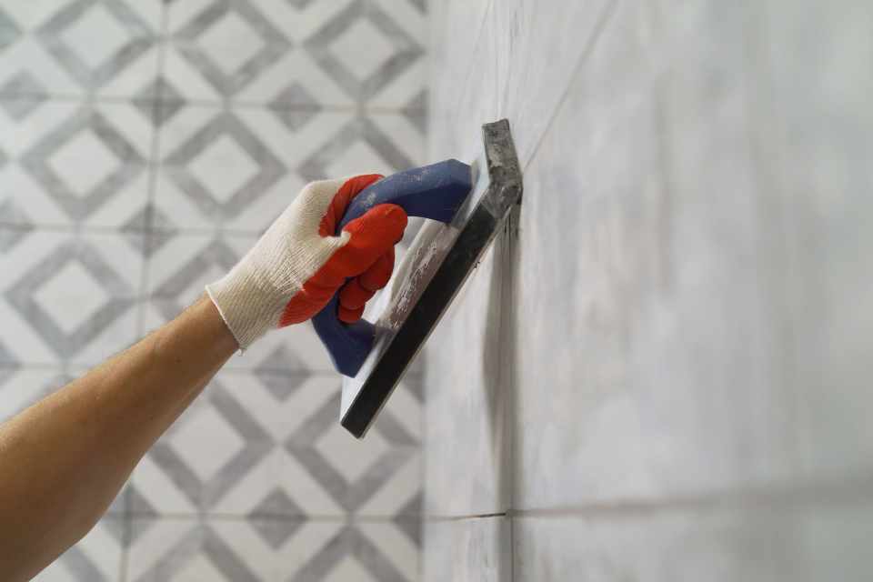 filling in grout with applicator on gray tiled walls
